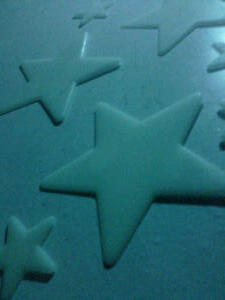 Glow in the dark stars catch the blue light on the wall beside my bed.